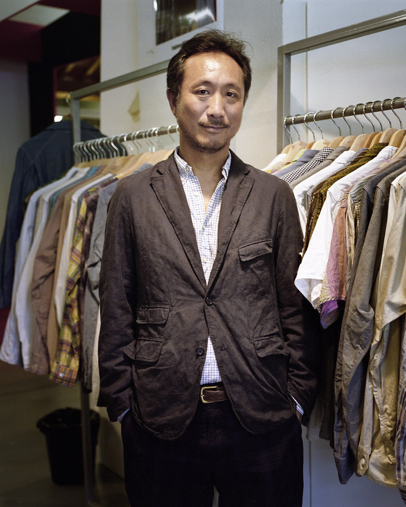 Daiki Suzuki, director of Engineered Garments, standing in front of clothing racks at Pitti Uomo.
