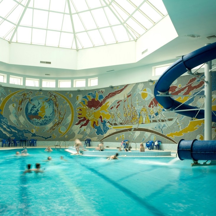 Interior of swimming pool at Hotel Belarus with colorful Soviet-style mural and water slide.