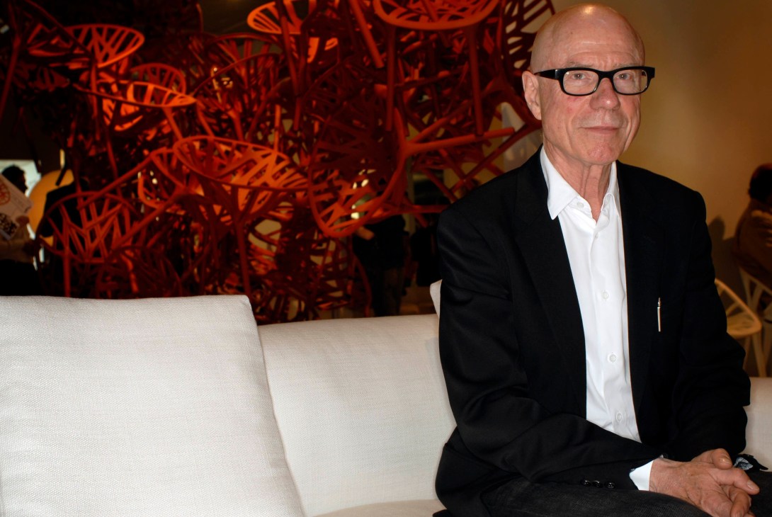 Rolf Fehlbaum, CEO of Vitra, sits on a white sofa in front of red decorative lighting.