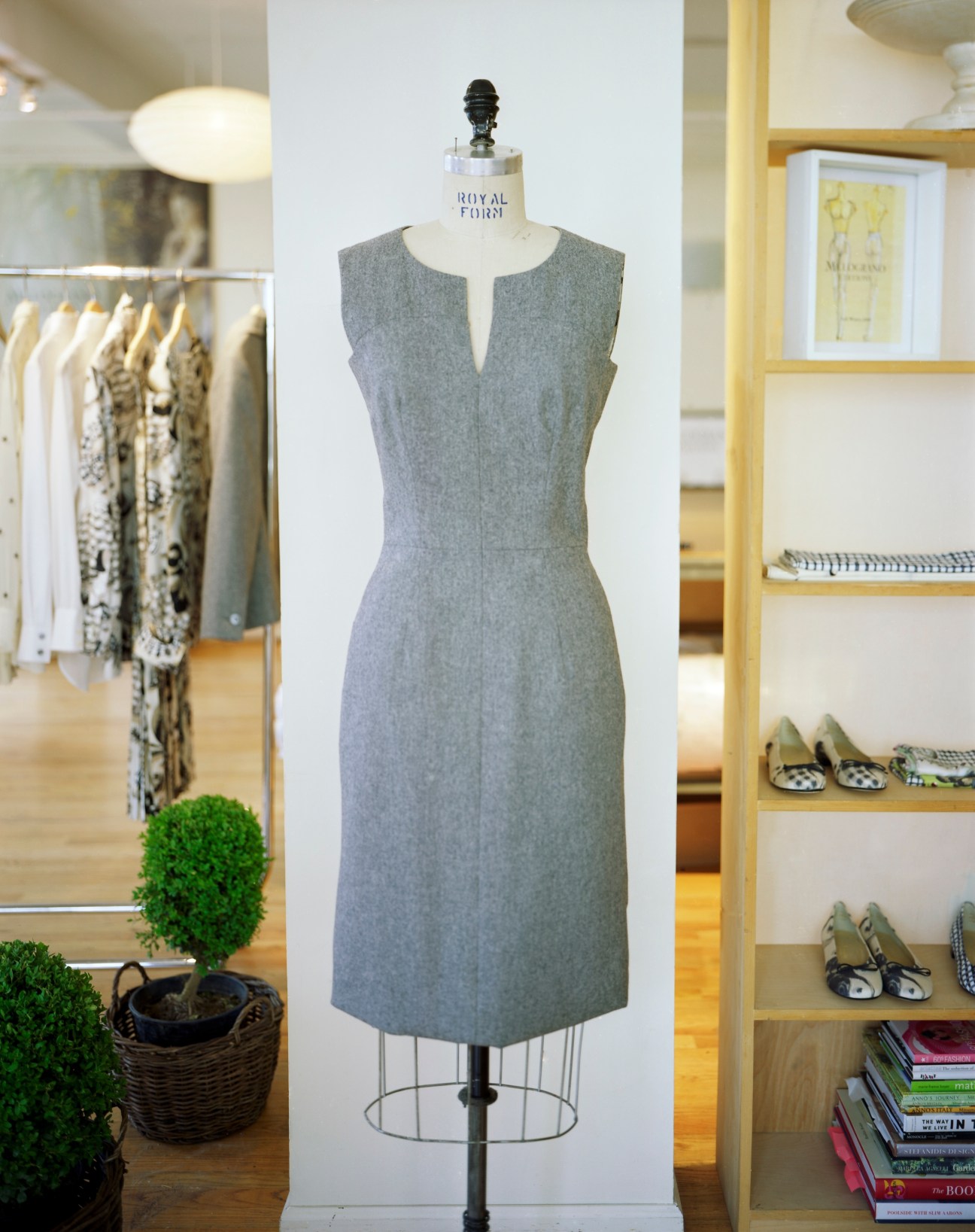 Grey sleeveless dress on mannequin in Melograno Editions retail space with shelving and clothing displays.