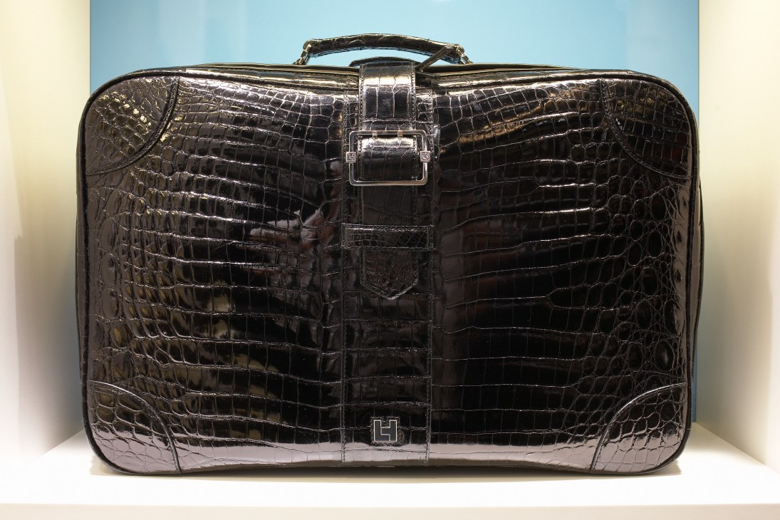 Black crocodile-embossed leather briefcase with silver hardware and carrying handle against neutral background.