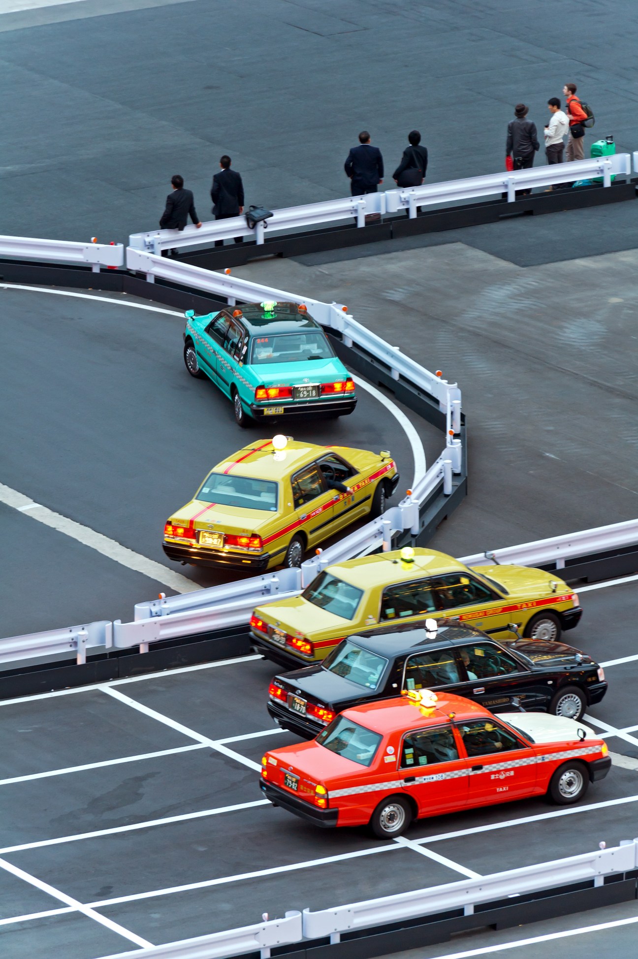 Multiple colorful Tokyo taxis lined up on a street at Tokyo Station with pedestrians walking nearby.