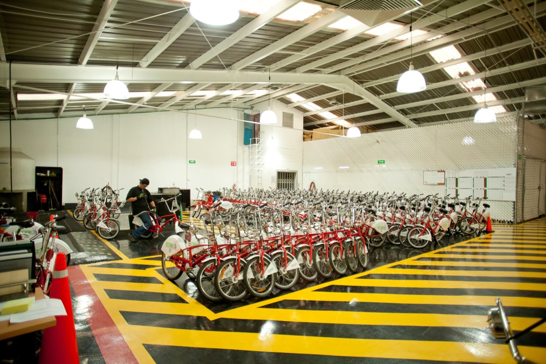 Red and white bicycles parked in rows at the Ecobici bikesharing headquarters facility.