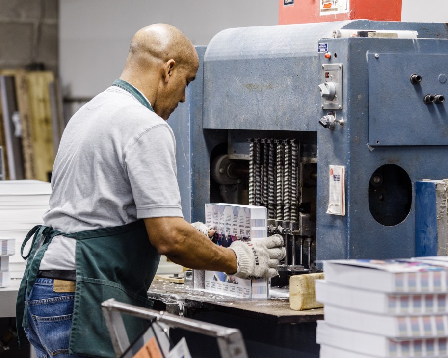 Worker in apron operating blue Pantone printing machine stacking finished graphic fan decks