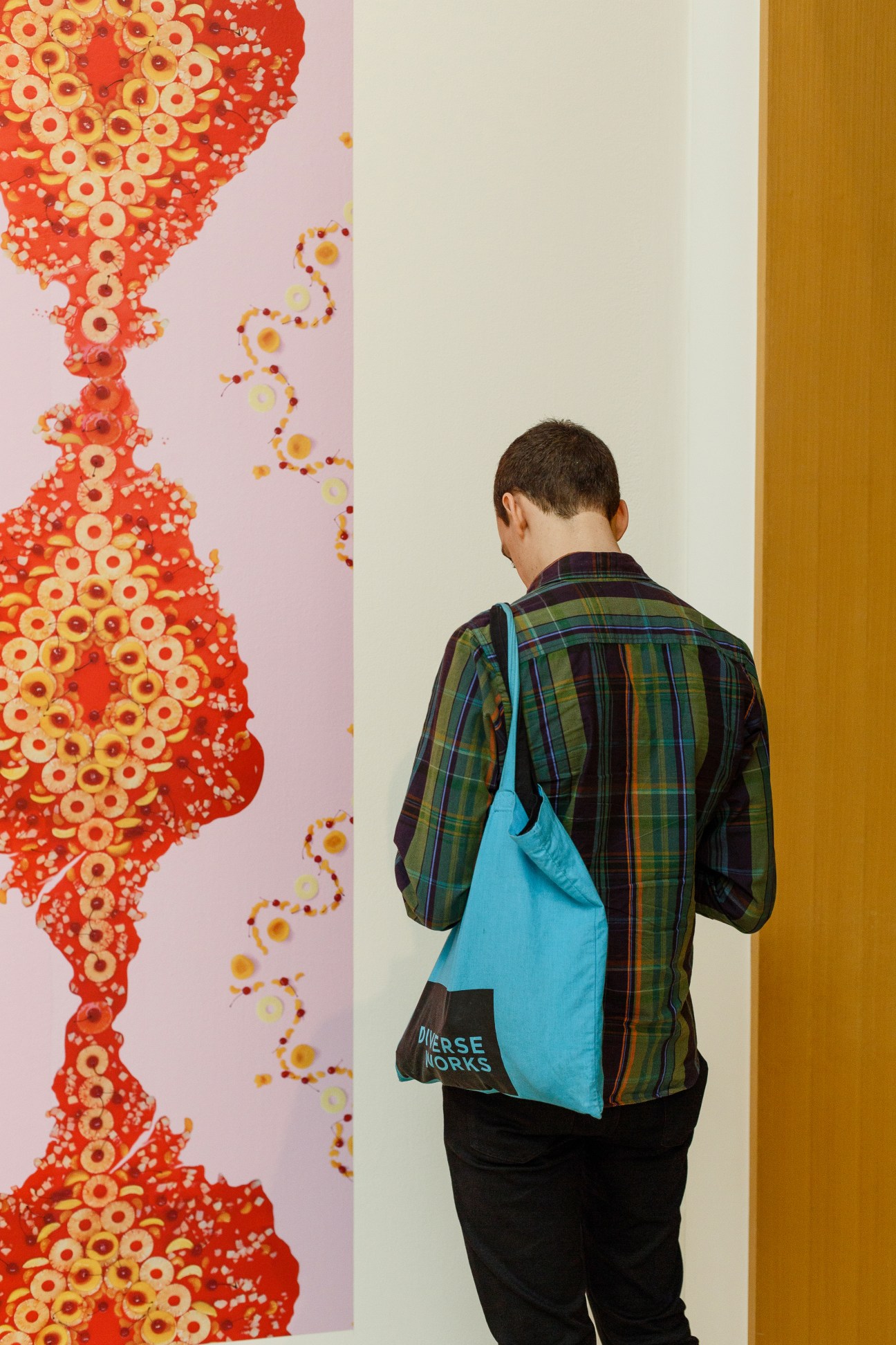 A visitor wearing a plaid jacket and blue bag views abstract artwork featuring red and orange circular patterns at San Jose Museum of Art.