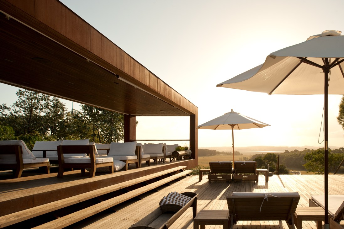 Wooden sundeck with lounge chairs, umbrellas, and covered seating area overlooking pastoral landscape at sunset.