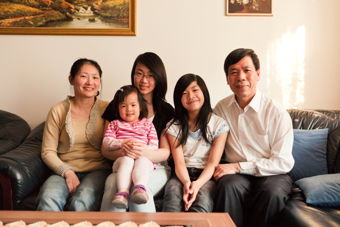 Nguyen Quoc Hung sits with his family on a sofa, including his wife, children, and a young grandchild in pink clothing.