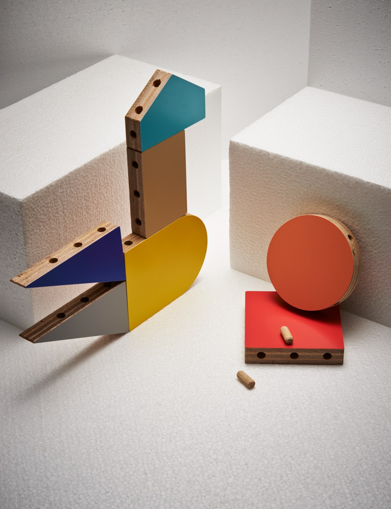 Koloro building blocks with coloured plywood shapes and wooden dowels on white surface.