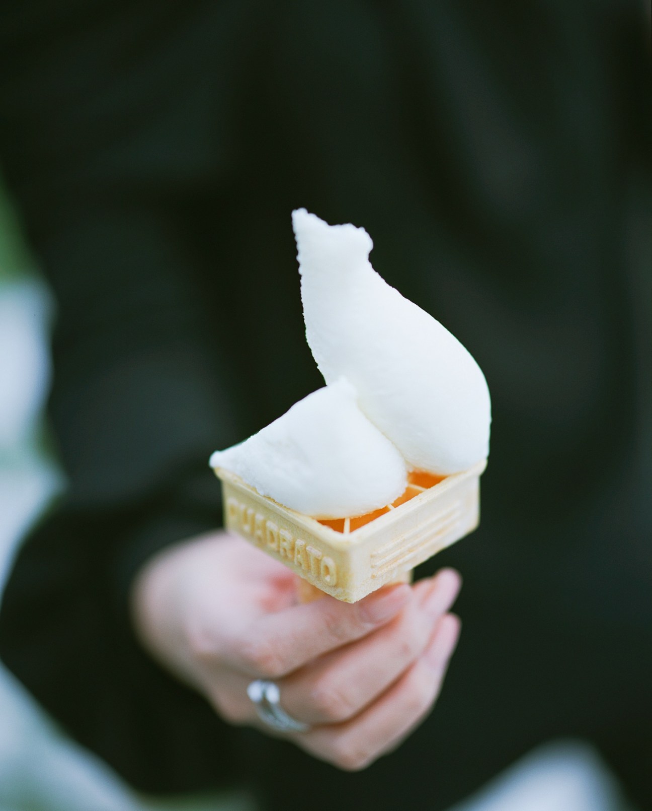 Hand holding a soft-serve ice cream with white swirl and orange center against dark background.