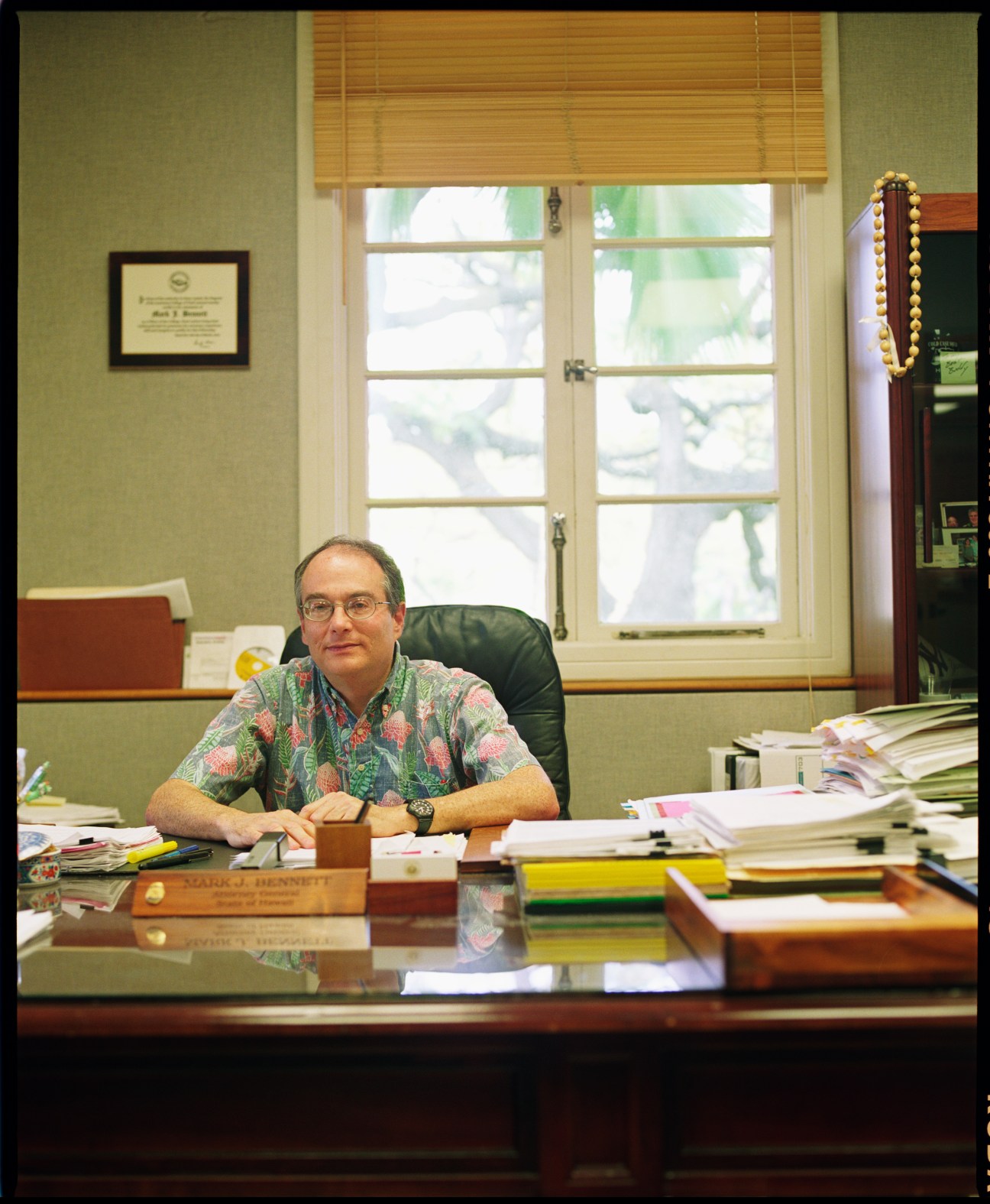 Mark Bennett, attorney general of Hawaii, sits at his desk in an office with green walls and large windows.