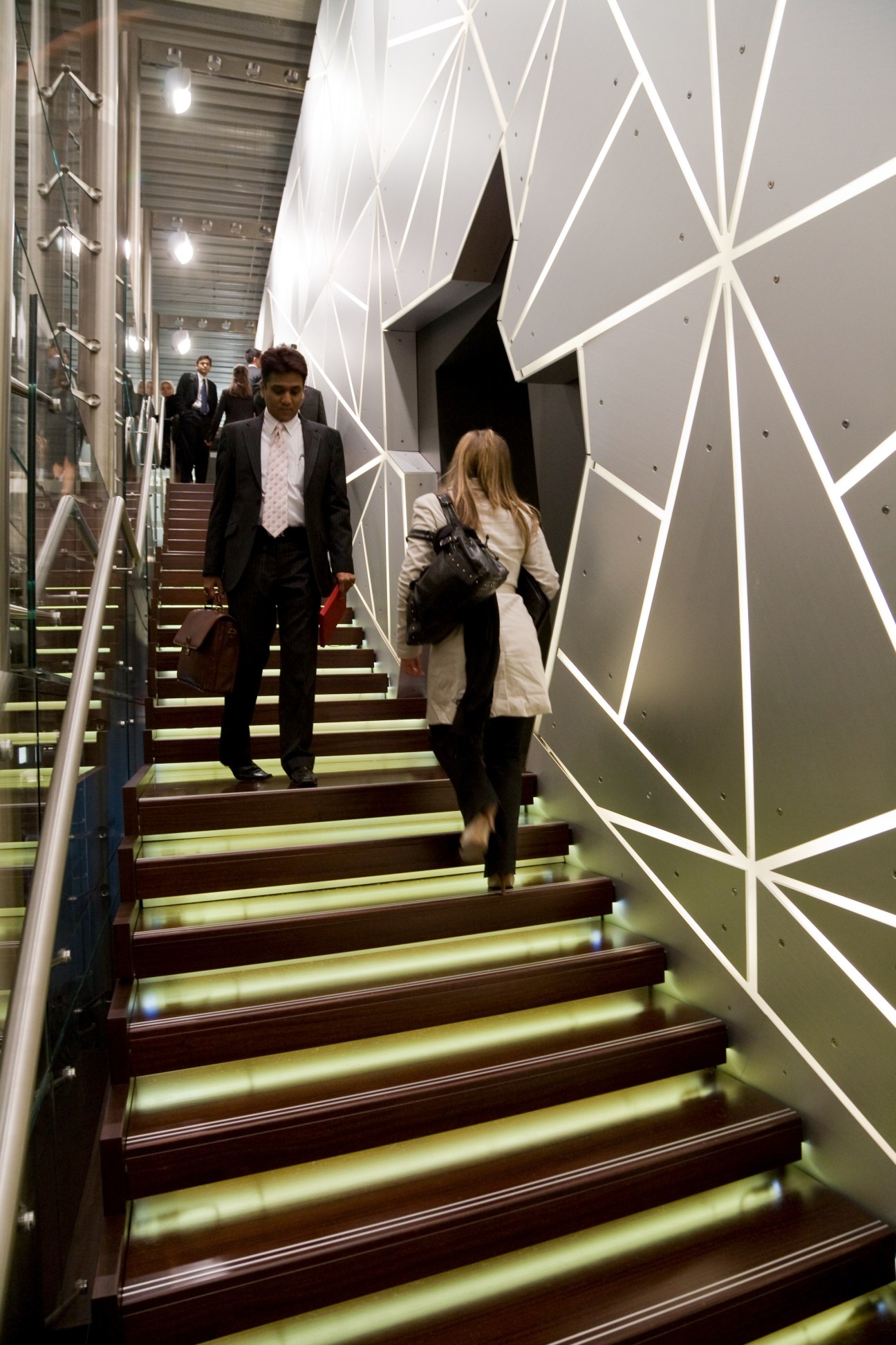 Visitors ascending an illuminated staircase in TAG Heuer's booth with geometric white wall design.