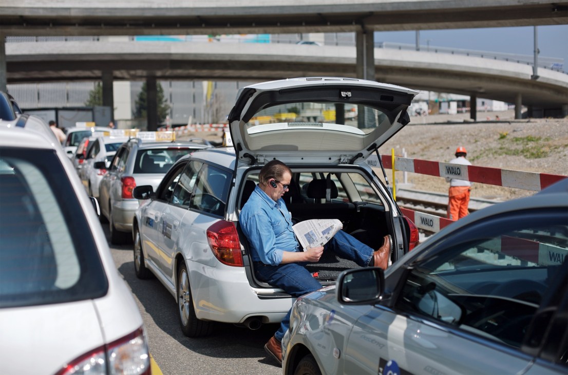 Taxi driver Rolans Schüpbach waits in his white Subaru Legacy at Zürich-Kloten Airport.