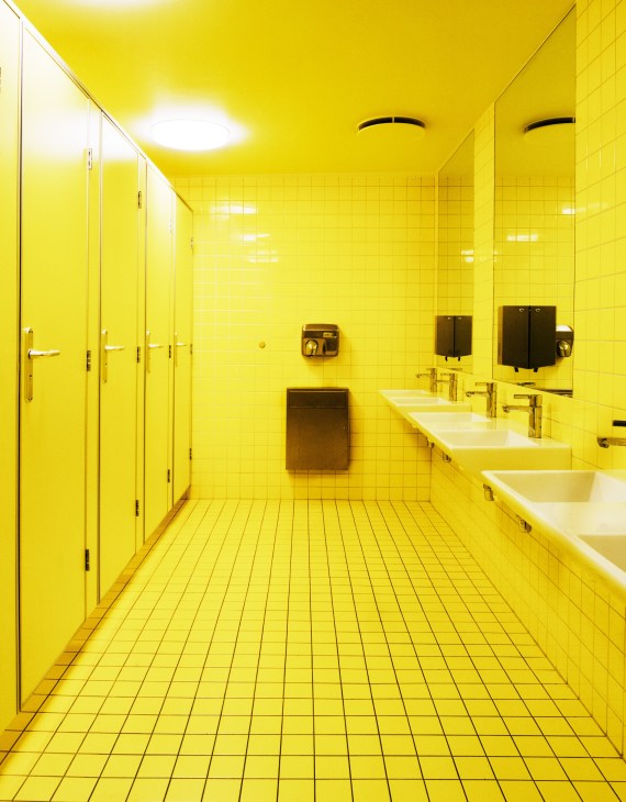 Boys' bathroom at Oslo International School with bright yellow tile walls, floor, and stalls.