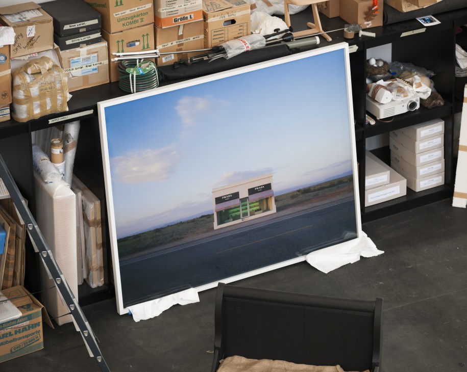 Printed photograph of Prada Marfa displayed in Elmgreen + Dragset's Berlin studio surrounded by cardboard boxes and materials.
