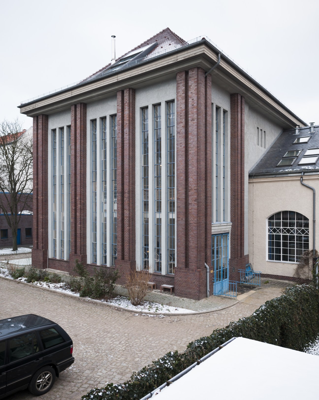 Renovated brick and white pumphouse studio building with tall windows in Berlin's Neukölln district.