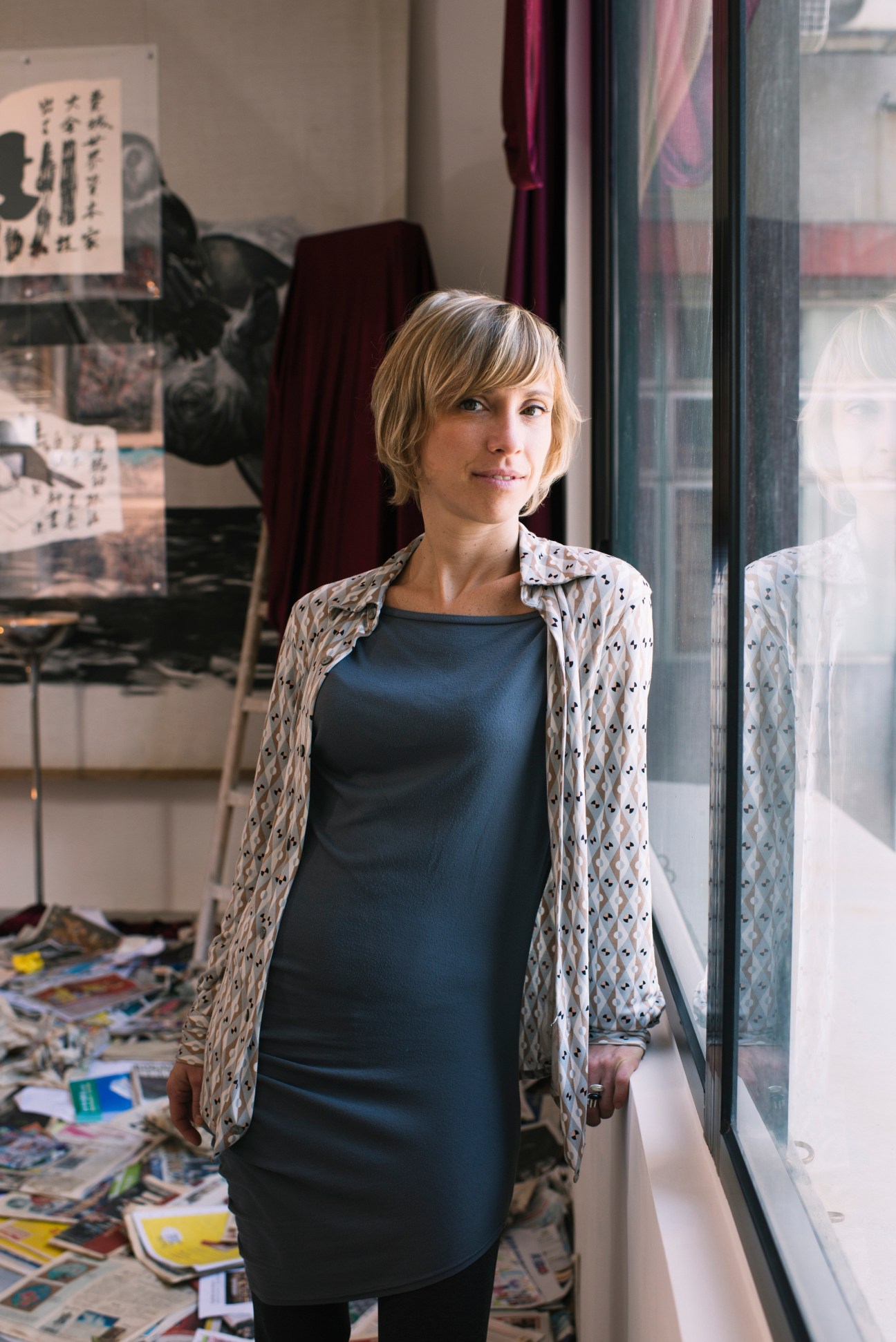 Woman standing in an art gallery space with Asian artwork and cultural materials visible in the background.