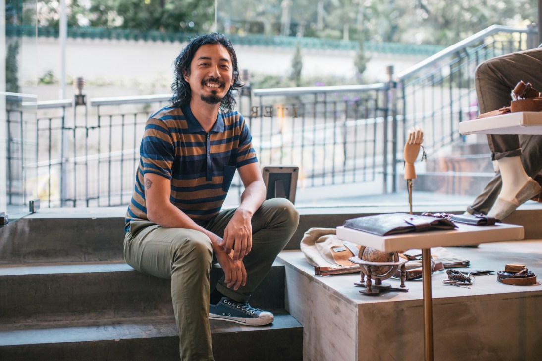 Iter Hominis manager Kapil Tamang sits smiling at the Hong Kong menswear shop, wearing a striped polo shirt.