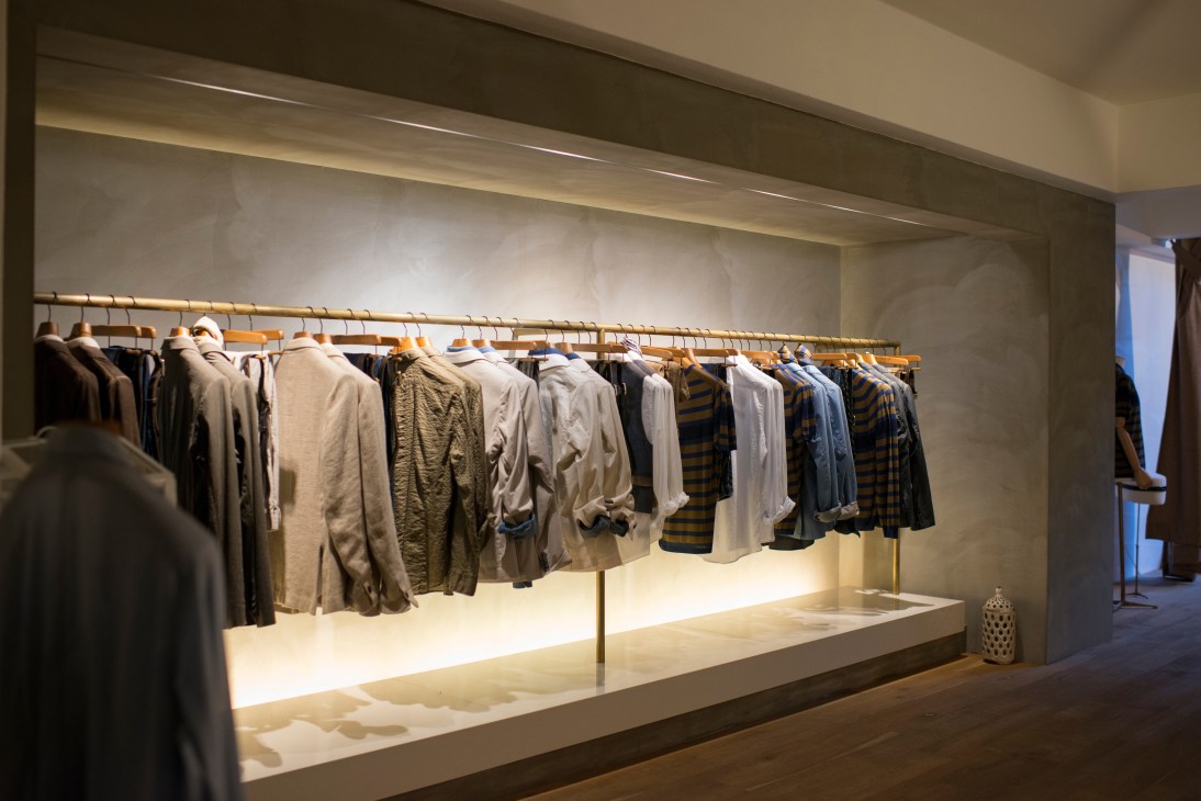 Interior of Iter Hominis menswear shop with clothing displayed on wooden hangers against illuminated wall.
