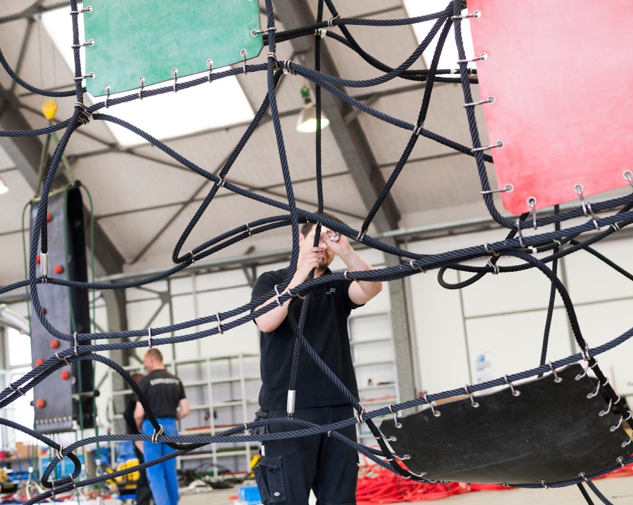Worker assembling dark navy ropes and metal connectors in Corocord's Berlin factory hall.