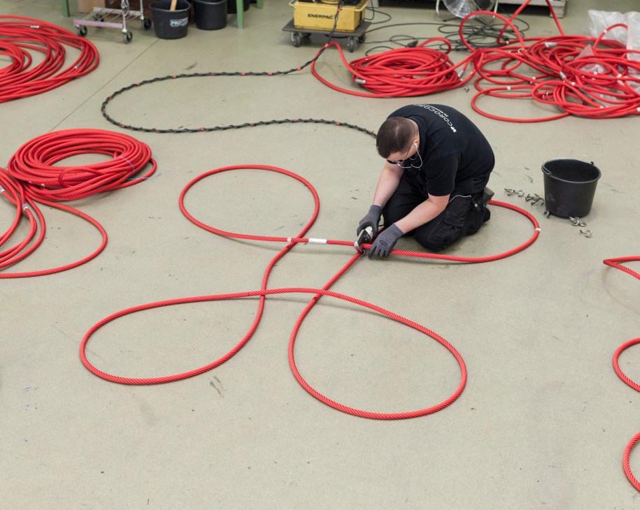 Worker assembling large red rope loops on factory floor for Corocord playground nets.