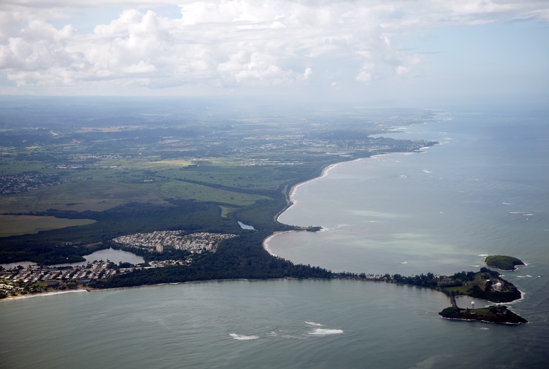 Aerial view of Puerto Rico's coastline showing beaches, forests, residential areas and ocean.