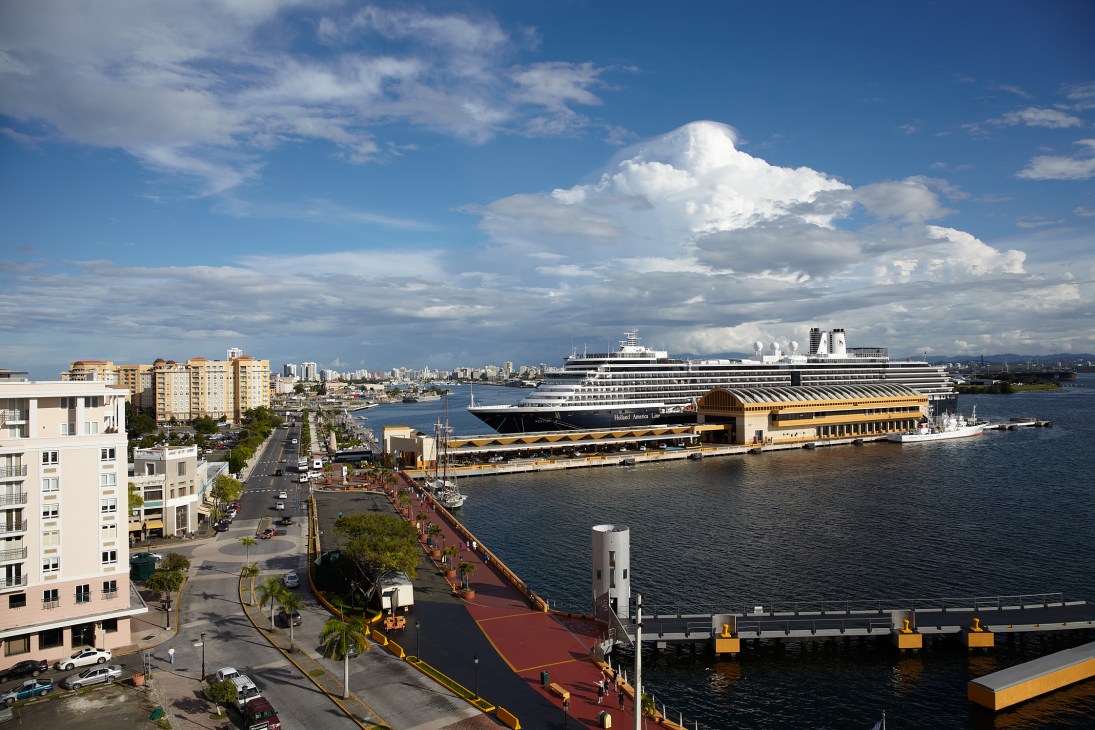 A large cruise ship docked at San Juan's terminal with waterfront buildings and cityscape visible.