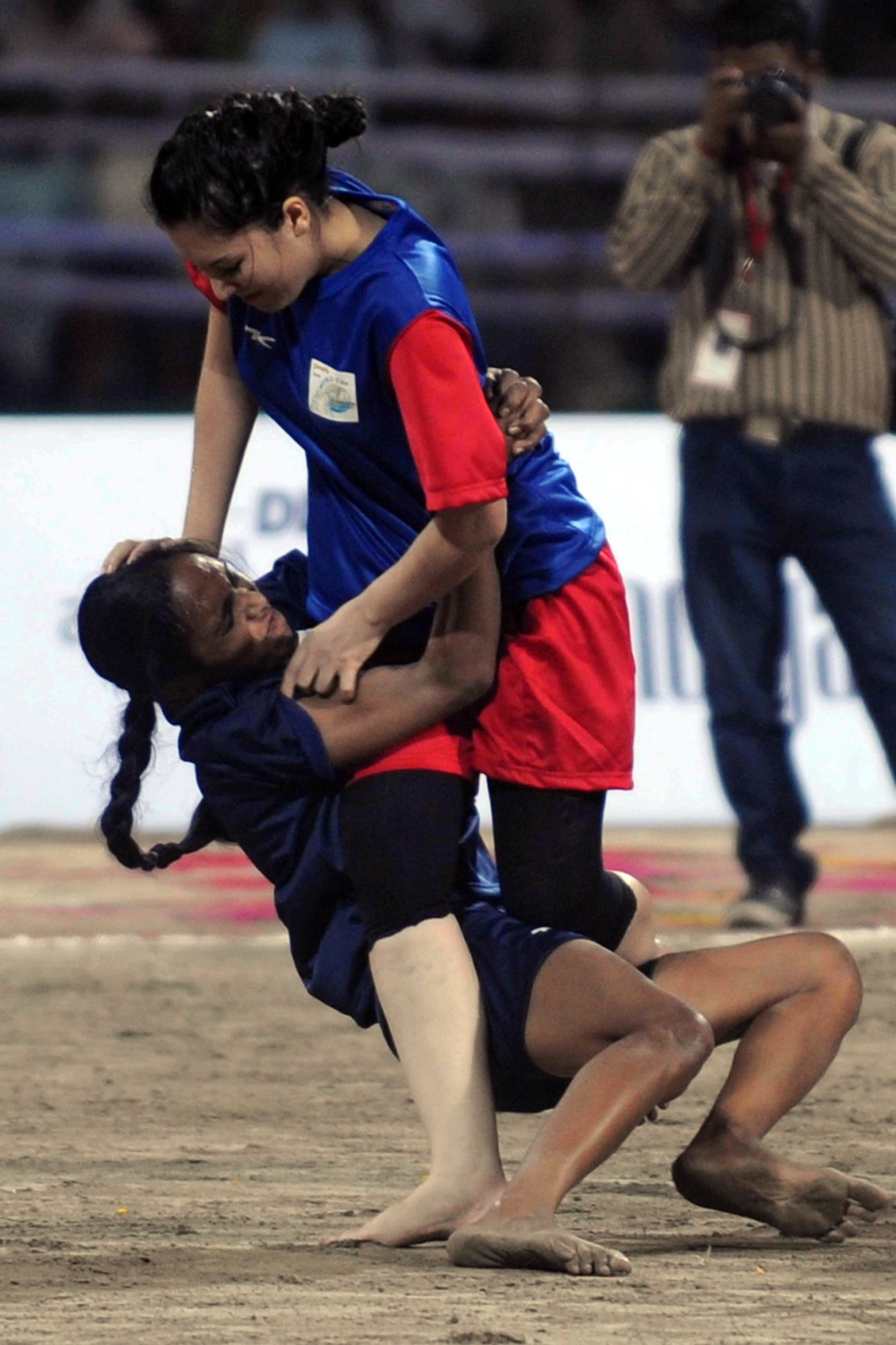Female kabaddi player in blue and red uniform grappling with opponent during World Cup match in India.