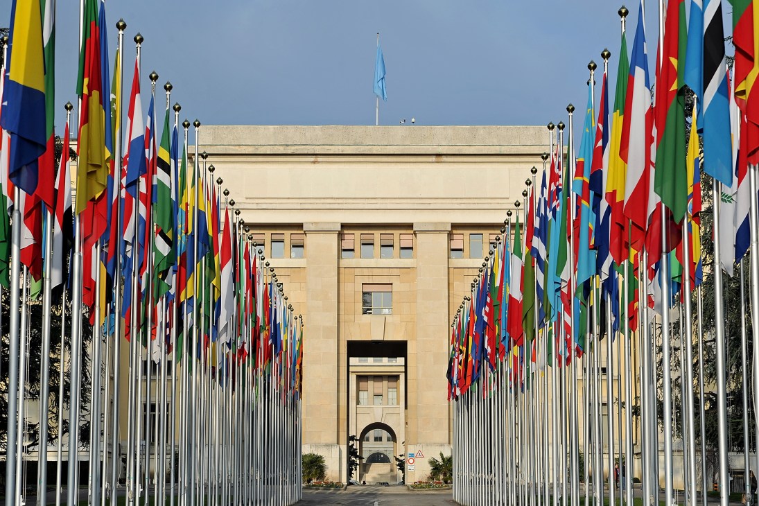 The Palais des Nations in Geneva with international flags lining the entrance approach.