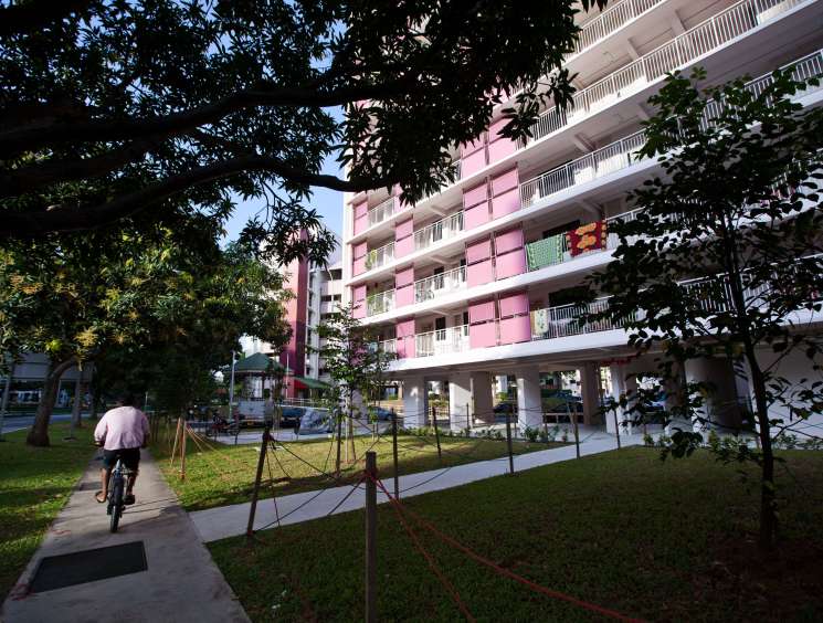 Modern pink and white apartment building with ground-level retail and landscaped grounds in Singapore.