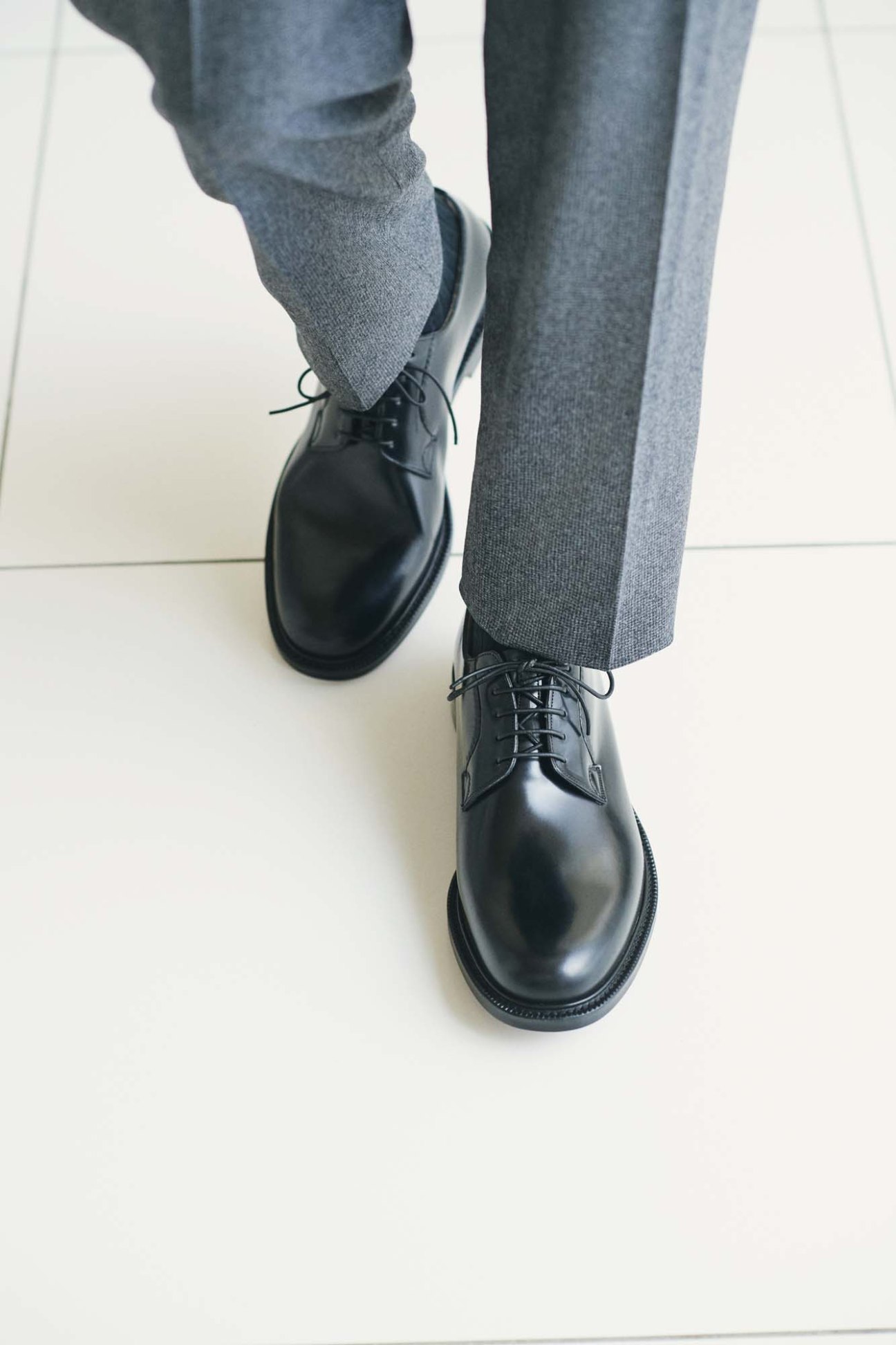 Person wearing gray socks, Canali trousers, and Church's black leather oxford shoes on white floor