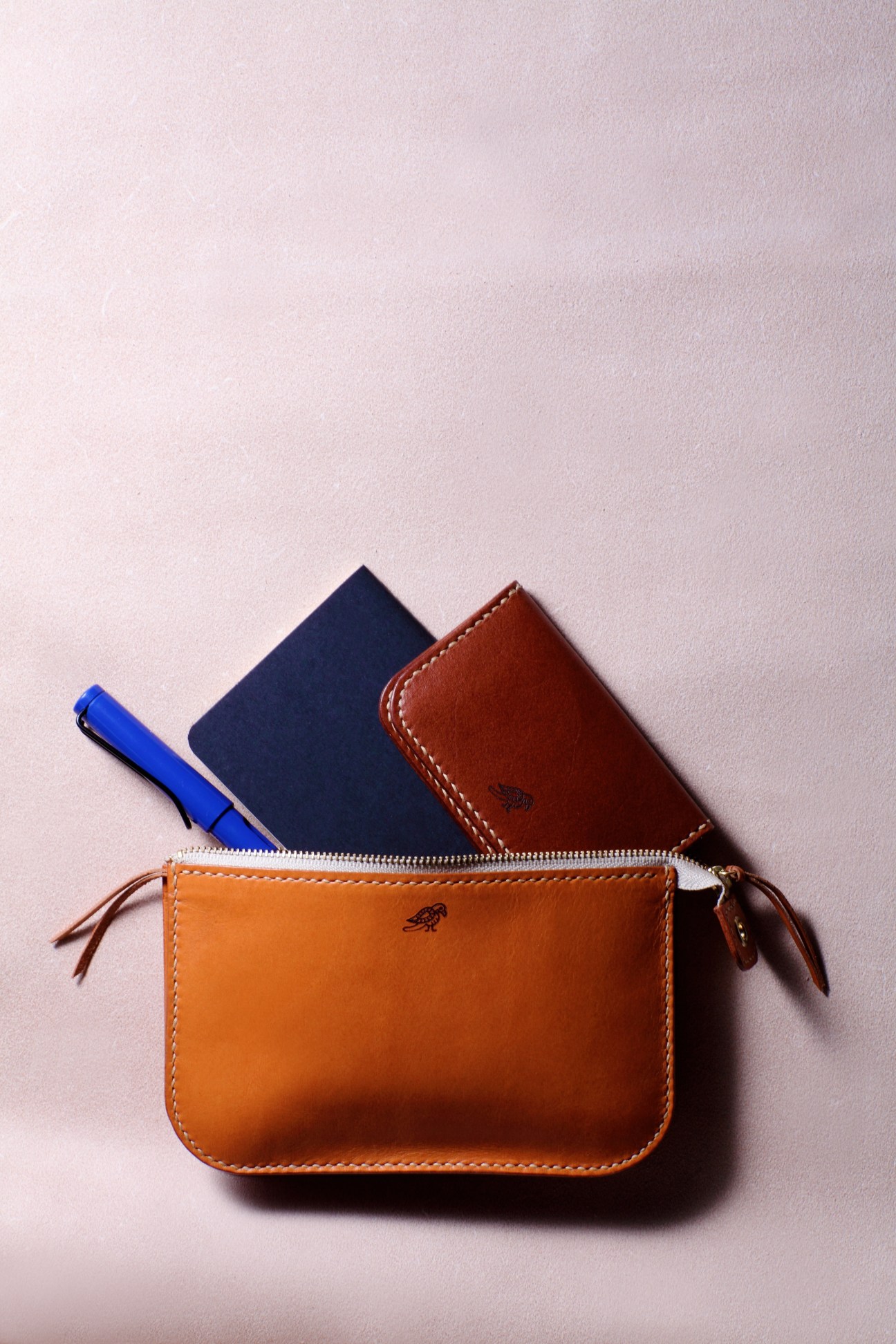 Rhythm leather wallets and accessories in orange, brown, navy and blue with contrasting stitching displayed on a pale background.