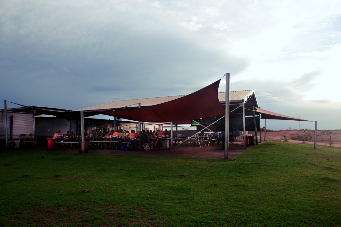 Miners in orange safety vests gather at the Wet Mess pub at Woodie Woodie mine site under a red awning.