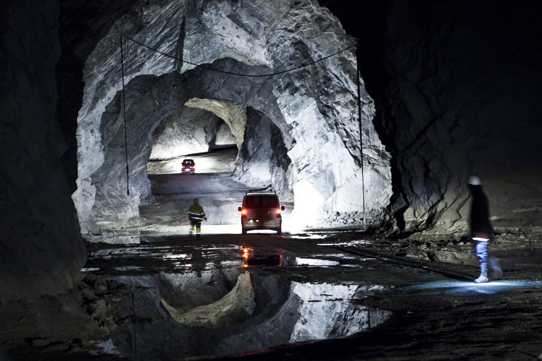 Vehicles driving through a converted mine tunnel with rocky walls and water reflections.
