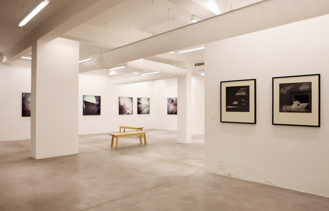 Minimalist white-walled gallery space with framed photographs displayed and wooden bench seating.