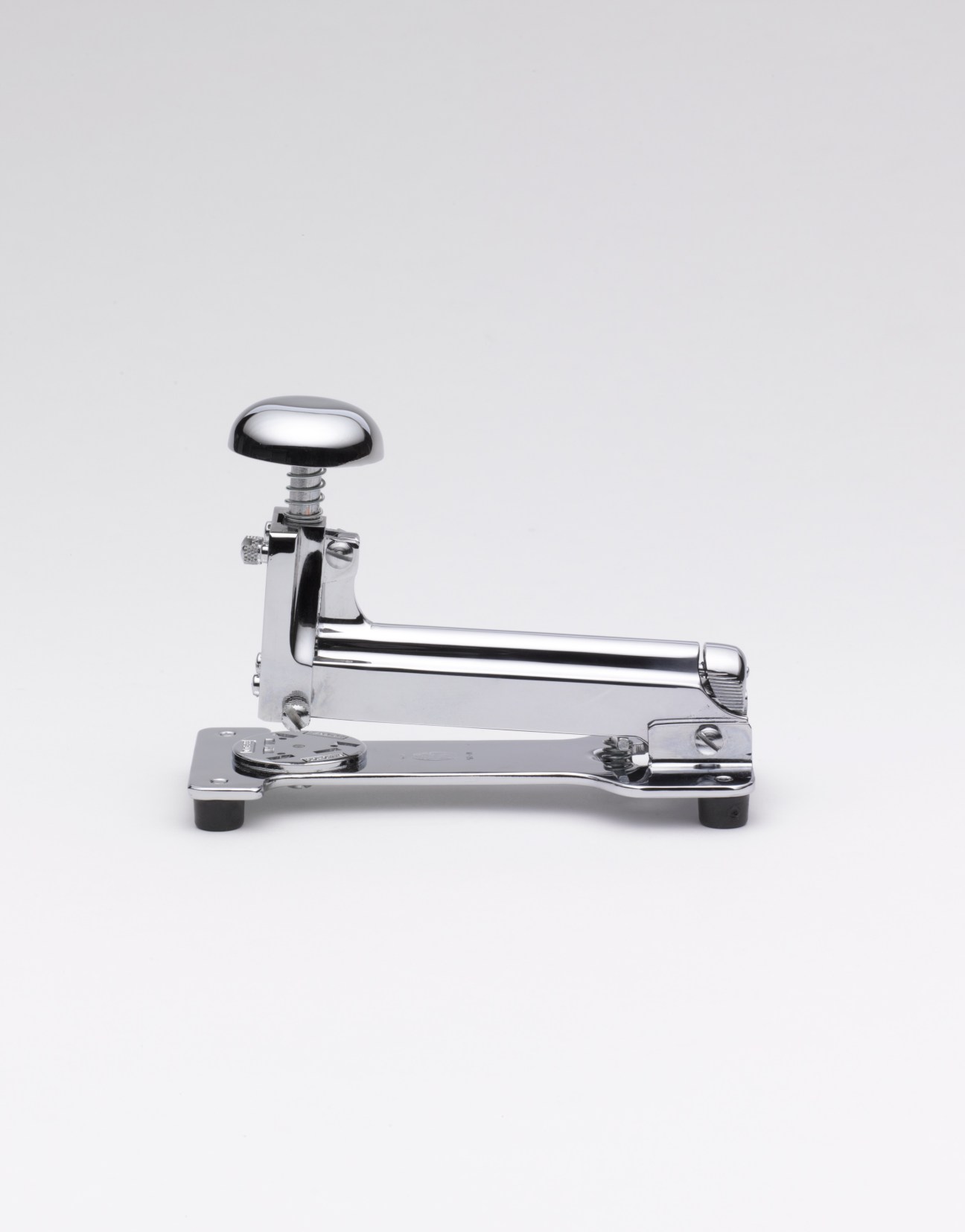 Chrome and black El Casco stapler with rounded top and lever handle on white background.