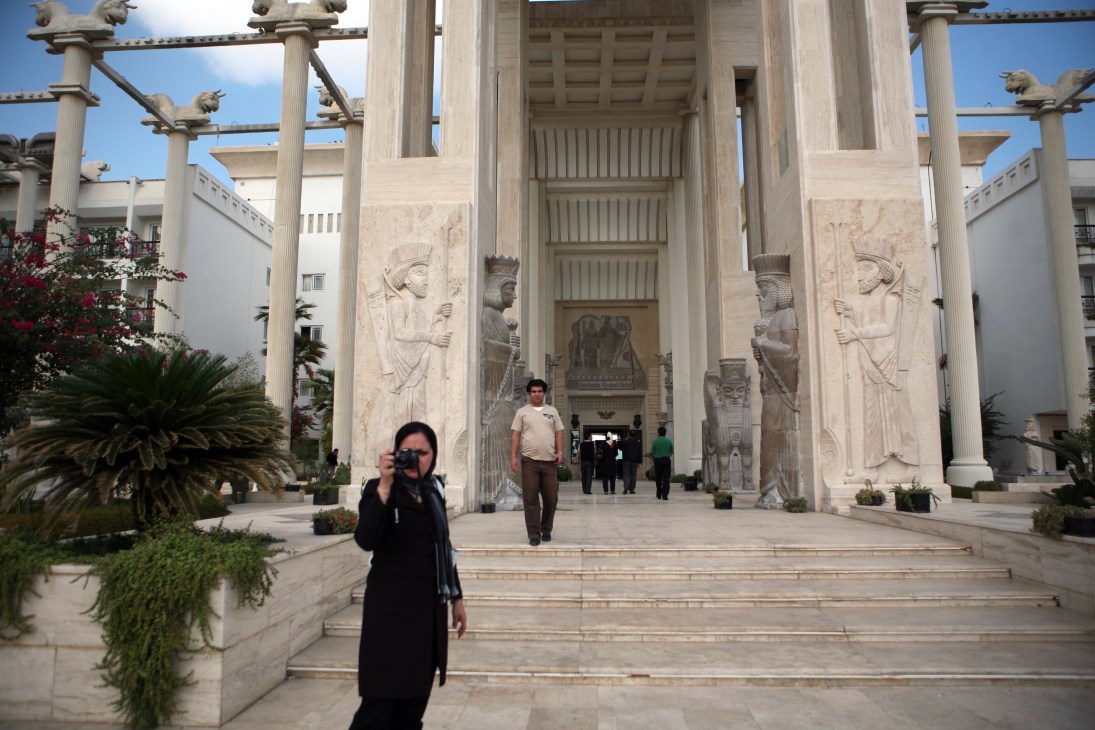Woman in black hijab photographs Persian architectural columns and friezes at the Dariush hotel entrance.