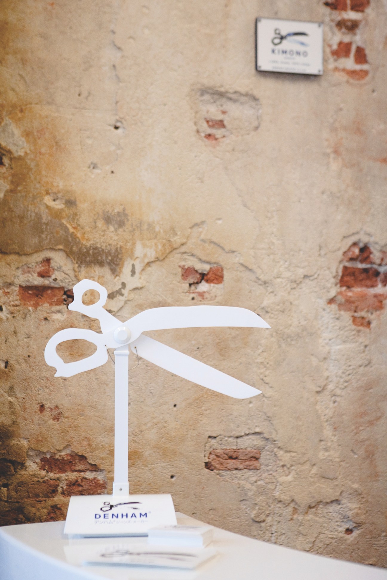 White decorative scissors display against weathered brick wall at Denham store.