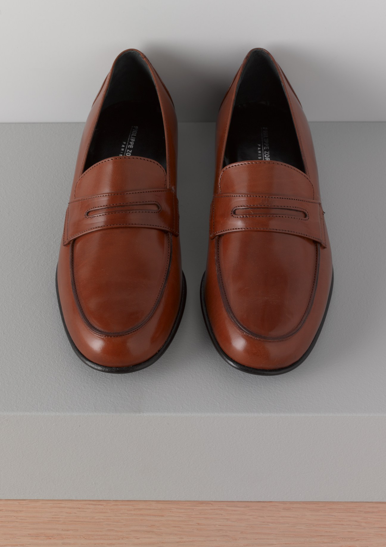 Pair of cognac-brown leather loafers with penny strap detail, viewed from above.