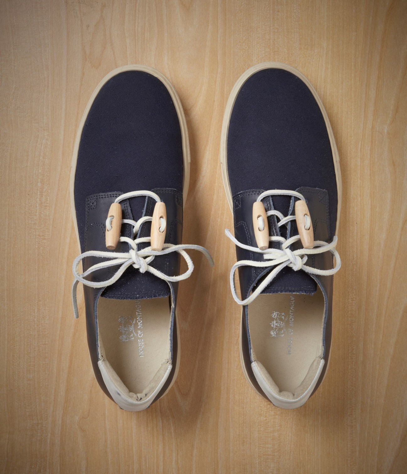 Pair of House of Montague navy canvas sneakers with white laces and wooden eyelets on wooden background.