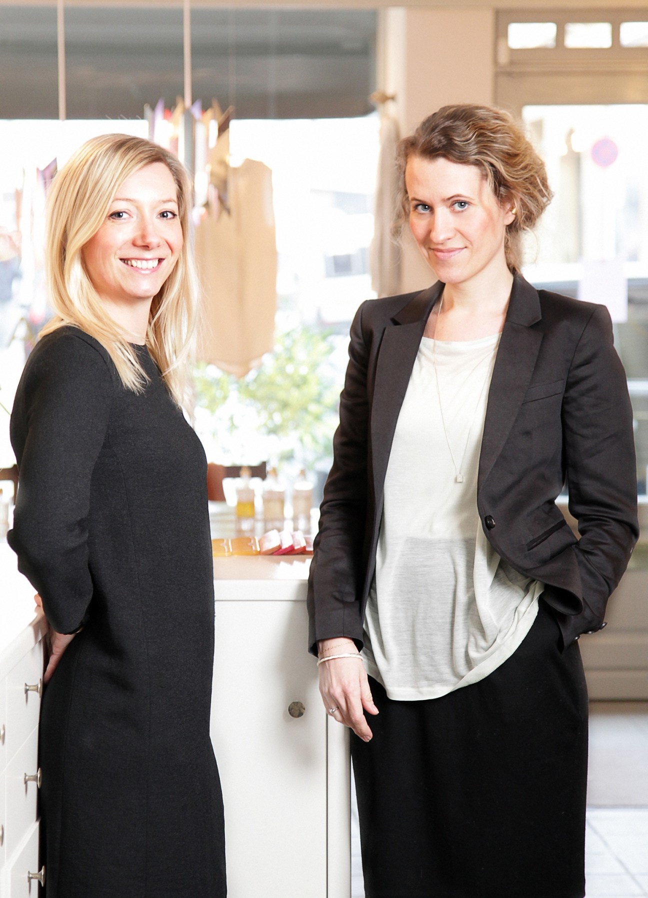 Two women posing in a bright retail space with product displays behind them.