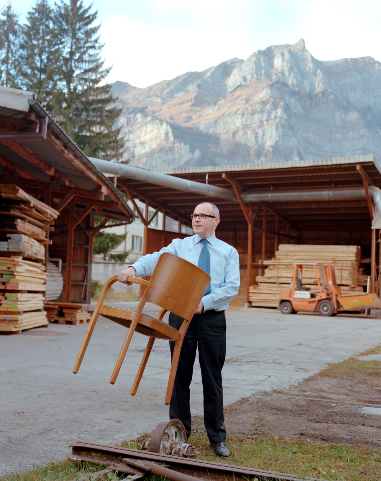 Markus Landolt holds a wooden chair at the Horgenglarus factory in Glarus, Switzerland, with mountains in the background.