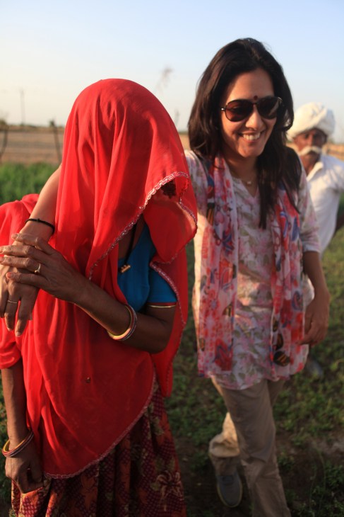 Chhavi Rajawat smiles while standing in a rural field with a local woman wearing a red headscarf.