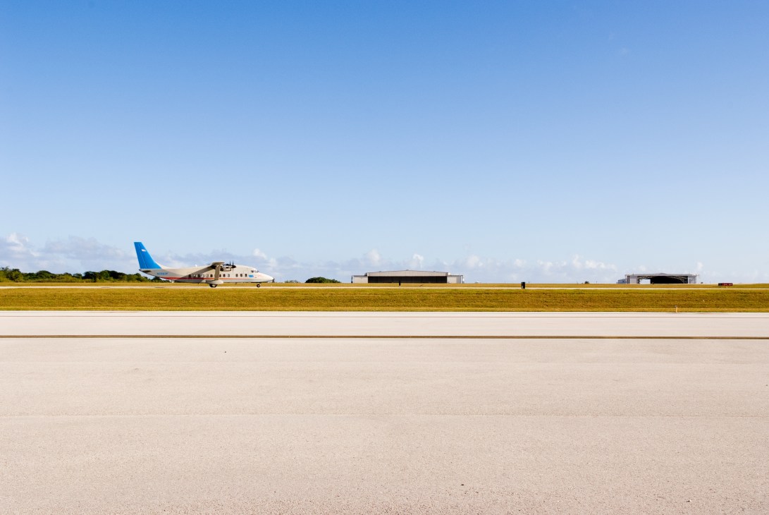Blue and white aircraft on runway at AB Won Pat International Airport with hangar buildings visible