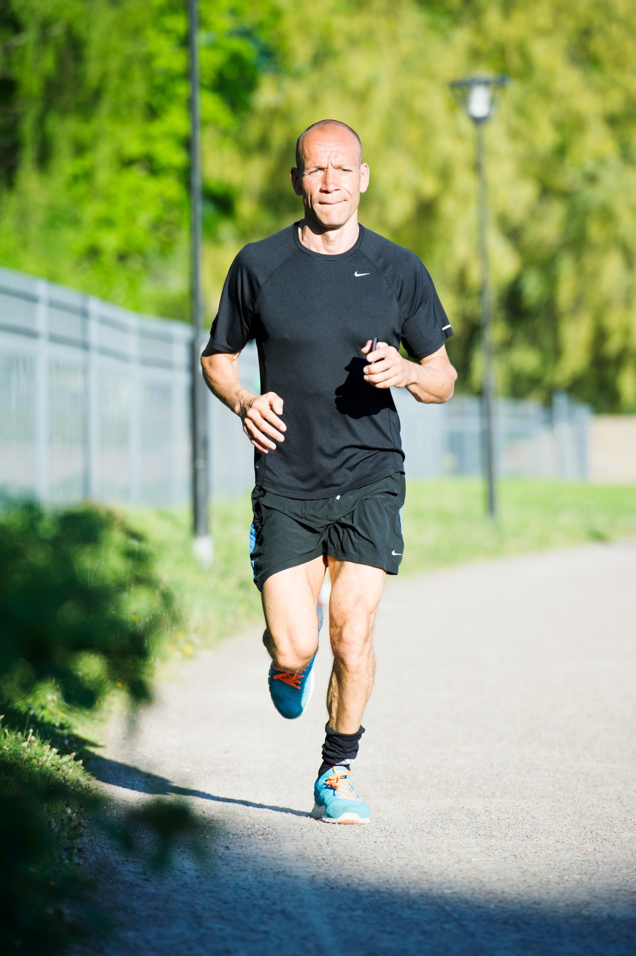 Man jogging on a path with green trees and fence in background.