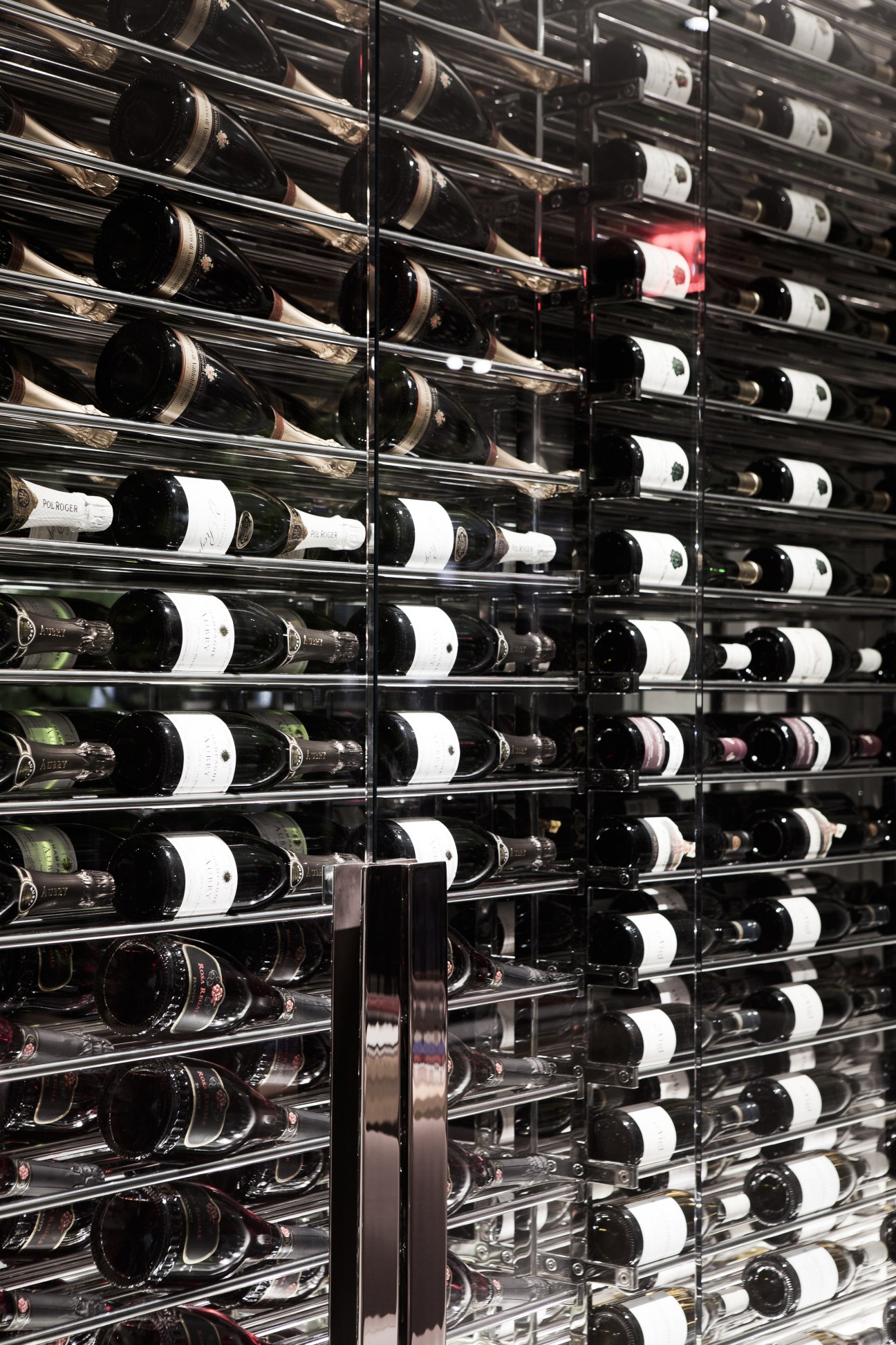 Floor-to-ceiling wine wall display with glass shelving holding numerous wine bottles with white labels at Andaz Fifth Avenue.