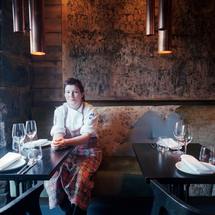 Owner/chef Vigdis Ylfa sits at a dining table in FiskeFelagid restaurant, wearing a white shirt and patterned apron.
