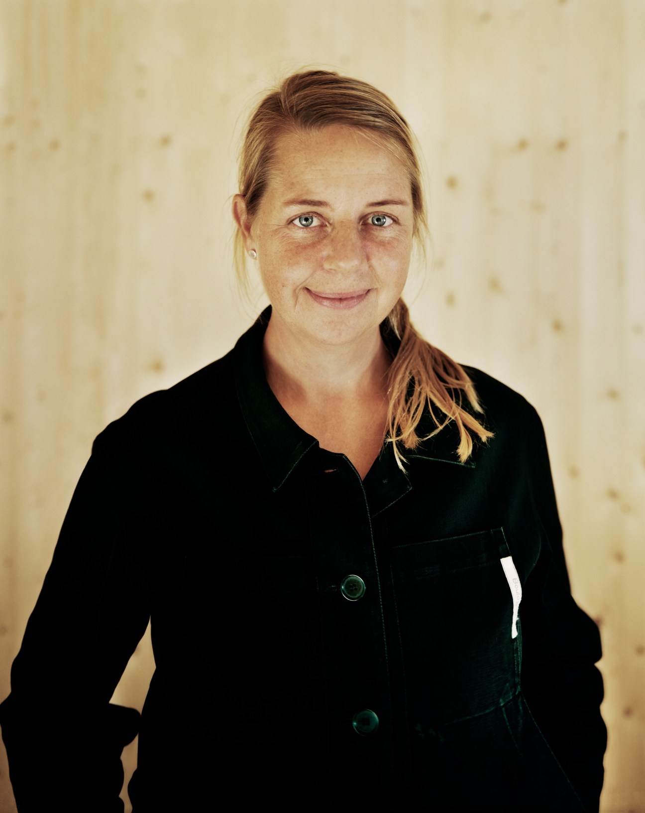 Portrait of Helena Bloom, co-owner of Leva Husfabrik, wearing a black blazer against a textured beige background.