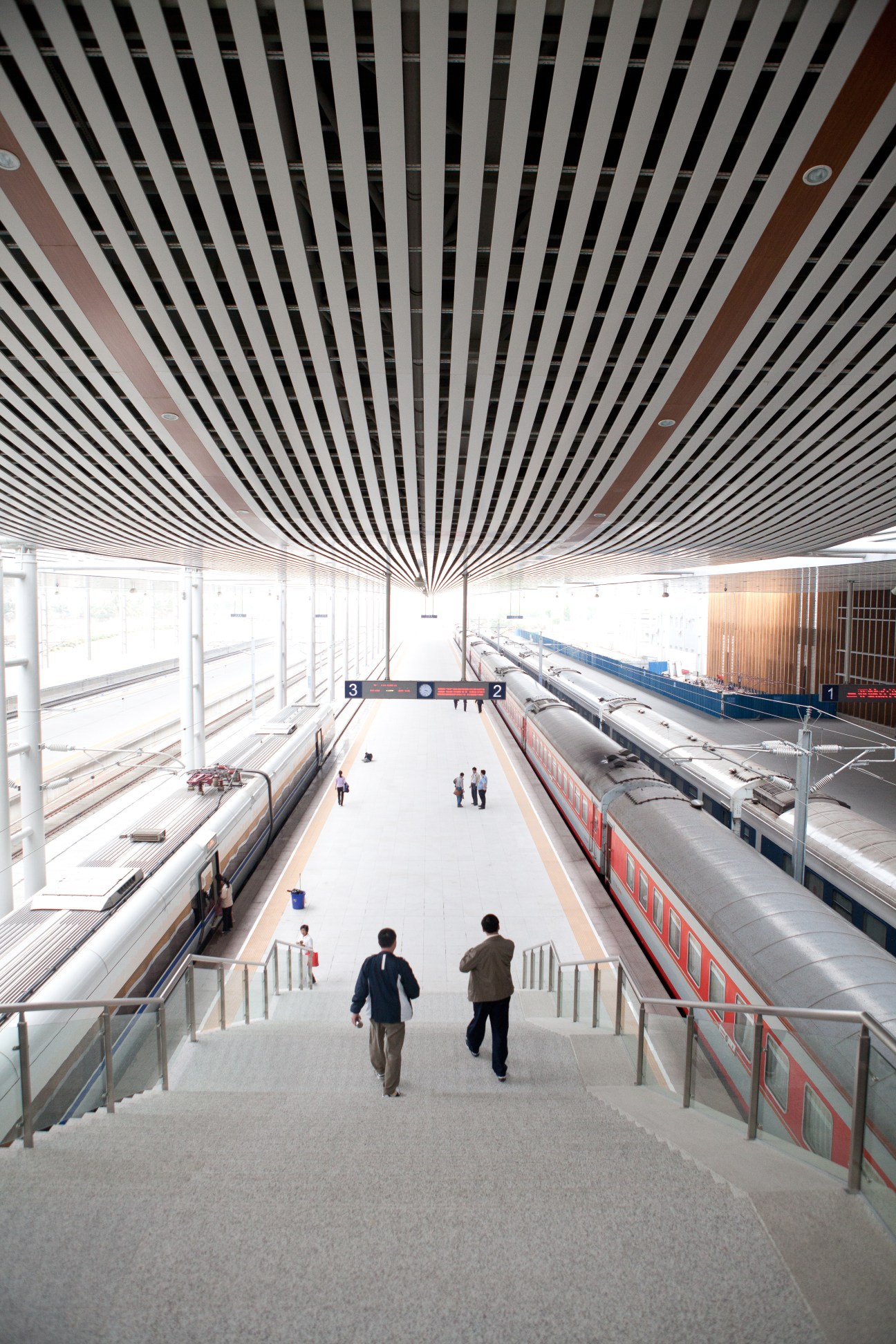Interior view of Sanya's new train station with high-speed trains at platforms below and passengers on stairs.