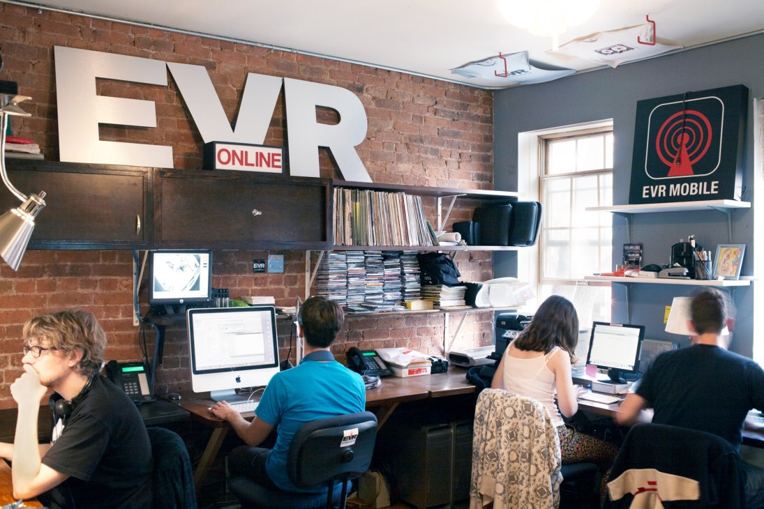 Staff working at desks in EVR's office with exposed brick walls and large EVR signage.