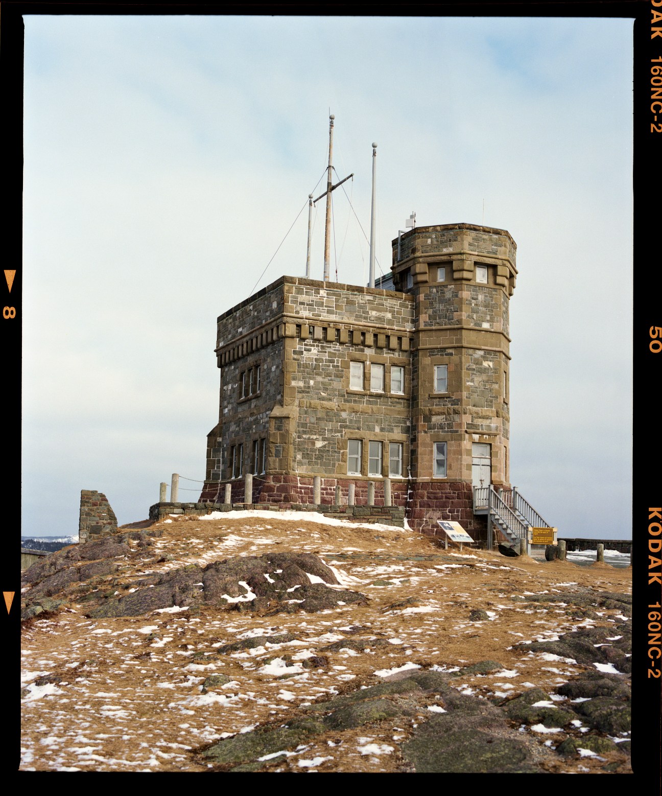Historic stone tower with turret on rocky hilltop with sparse snow patches